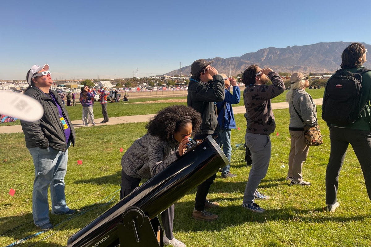 A crowd watching a solar eclipse through ISO-certified eclipse glasses, one person at a filtered telescope