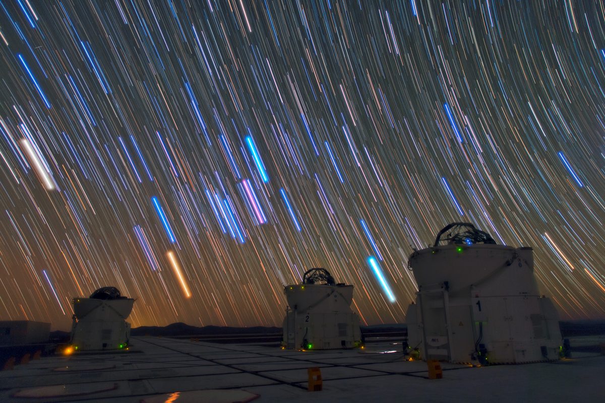 Long-exposure star trails above three telescope domes, every star a line instead of a point